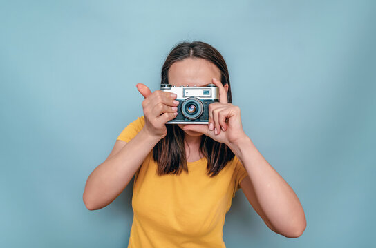 Woman takes pictures with an old film camera. Yellow boot cap, black hair, blue background