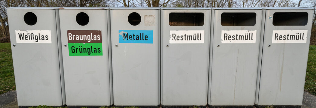 &Ouml;ffentlicher M&uuml;lleimer zur M&uuml;lltrennung in einem Park mit der Beschriftung Wei&szlig;glas, Braunglas, Gr&uuml;nglas, Metalle und Restm&uuml;ll