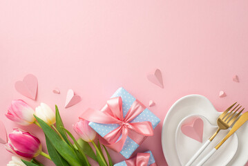 Festive Mother's day table arrangement. Top view flat lay of plates, cutlery, tulips, gift boxes, and decorative hearts on pastel pink background with a space for promotional content or text
