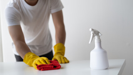 Close up view of man cleaning white wooden table using clothes and cleaning solution liquid spray.