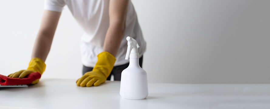 Close up view of man cleaning white wooden table using clothes and cleaning solution liquid spray.