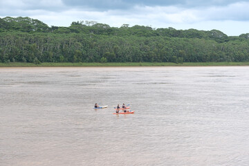 People canoeing kayaking on Amazon river with green jungle tree and sky at Puerto Maldonado Peru.