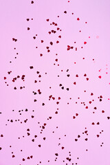 Many small red hearts on a pink background. Holiday concept. Flat lay for your design. Vertical image.
