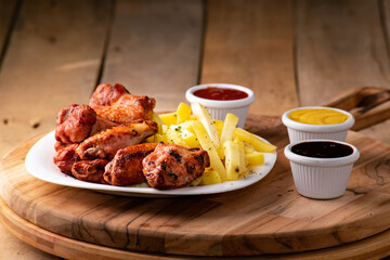 bbq chicken wings with french fries and ketchup, mustard and bbq on a rustic wooden table on a black background