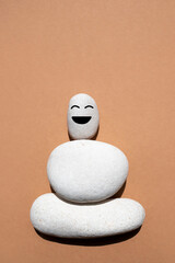 Three white smooth stones on top of each other on a beige background. Stone with a funny face. The...