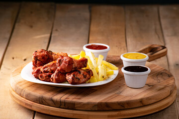 bbq chicken wings with french fries and ketchup, mustard and bbq on a rustic wooden table on a black background