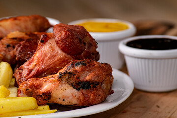 bbq chicken wings with french fries and ketchup, mustard and bbq on a rustic wooden table on a black background