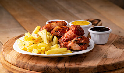 bbq chicken wings with french fries and ketchup, mustard and bbq on a rustic wooden table on a black background