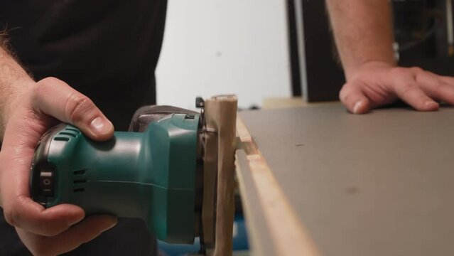 Worker grinds wooden workpiece edge with electrical tool in workshop closeup. Man making handmade furniture at plant. Handwork in carpentry shop