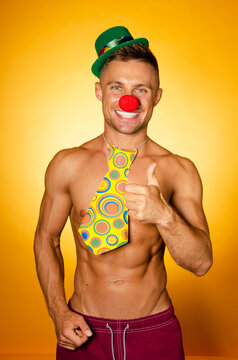 Young attractive man with an athletic body in a clown costume. Orange background.	