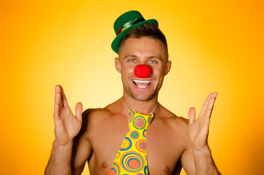 Young attractive man with an athletic body in a clown costume. Orange background.	