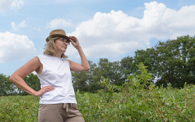 Young woman harvesting in a summer field. Hat with sun stripes, glasses.