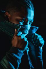Black man at night in the city among the signs. Photo in the dark. Afro-american man in jacket and bandana.