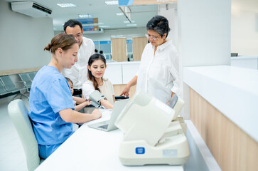 Obraz premium Caucasian nurse measure blood pressure of Asian woman and support by her family with husband, little girl and grandmother in area of hallway of hospital.