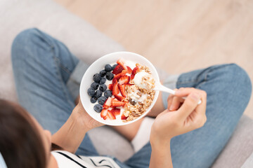Asian Woman having delicious healthy breakfast at home on morning. Health care female eats yogurt with granola and berry fruit. Healthy food, Vitamins, clean diet, dieting, detox, organic food.