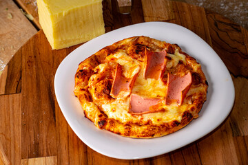 Pizza surrounded by peppers, tomatoes, mushrooms and a block of mozzarella cheese on a rustic wooden table against a black background