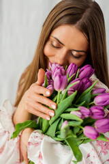 Portrait of sexy beautiful young woman with long hair. Model with a bouquet of lilac tulips on white. Spring. Holidays.