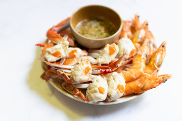 Steamed blue crab legs and shrimp on plate serving with spicy sauce.