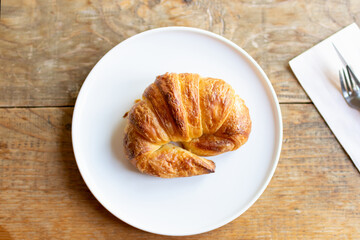 French croissant on plate on wooden table and nature sunlight with shadow through from window.