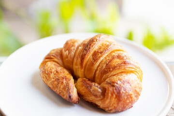 French croissant on plate on wooden table and nature sunlight with shadow through from window.