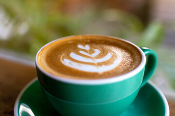 Cup of coffee with latte art on wooden table and morning sunlight with shadow through from window. Beautiful morning.