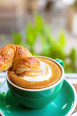 Cup of coffee with latte art with croissants on wooden table and morning sunlight with shadow through from window. Beautiful meal with warm sunlight.