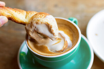Cup of coffee with latte art with croissants on wooden table and morning sunlight with shadow through from window. Beautiful meal with warm sunlight.