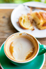 Cup of coffee with latte art with croissants on wooden table and morning sunlight with shadow through from window. Beautiful meal with warm sunlight.