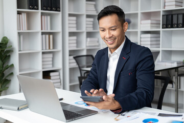Confident handsome businessman sitting at his desk while using the calculator for the project.