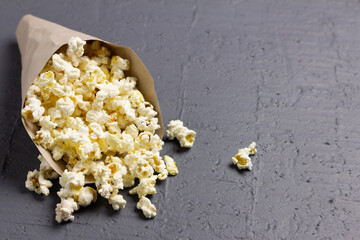 Eco-friendly paper cone filled with popcorn spilled on textured surface.