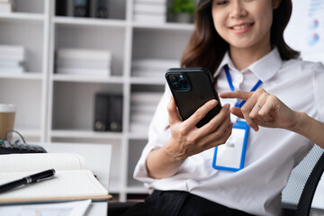 Beautiful Asian businesswoman using her smartphone in her office room, chatting with her friends.