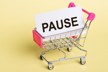On a light yellow background - a shopping cart with a white sticker with the text PAUSE