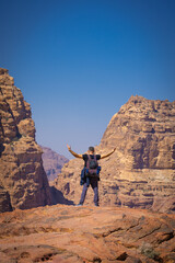 Petra w Jordanii. Mężczyzna stojący na szczycie skalnej góry na tle błękitnego, niebieskiego...