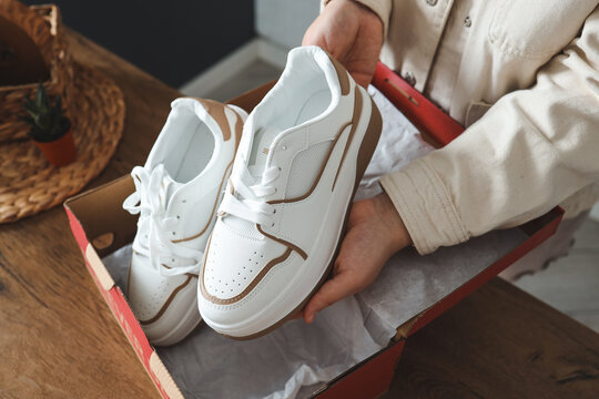 Unpacking women's shoes, stylish white sneakers in hands