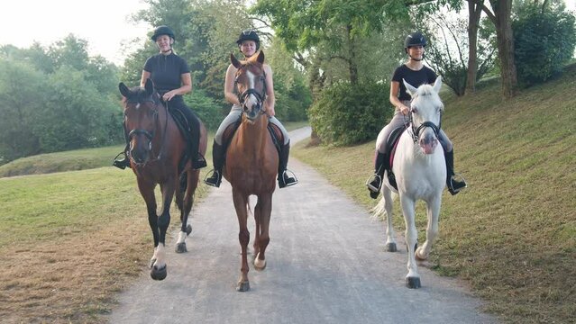 Front view of three female riders riding horses along the trail by the river, tracking shot. Recreation and leisure activity concepts.