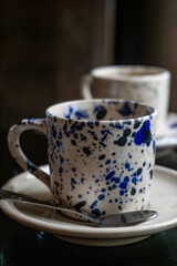 White coffee cup with blue spots on a saucer with a spoon on a wooden table