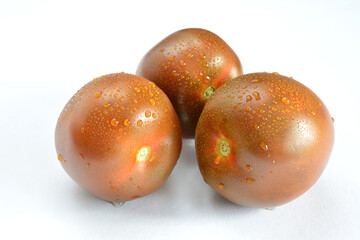 Three black tomatoes with water drops on them isolated on white background 