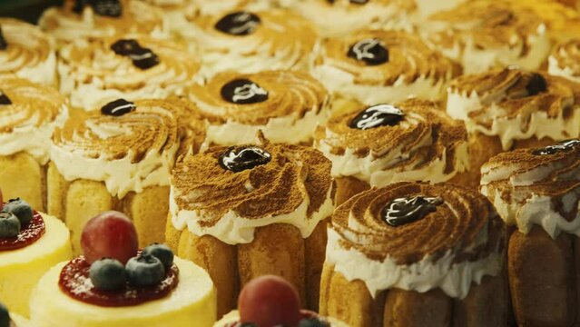 Cookies, cakes, eclairs with cream and fruit in a cafe behind a glass window. Different colors with sprinkled nuts and raisins.