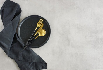 Empty black ceramic plate,linen napkin   and cutlery on gray stone background top view with copy...