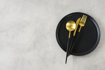 Empty black ceramic plate and cutlery on gray stone background top view with copy space . Modern kitchen utensils.Space for text or menu .Business food brand template.