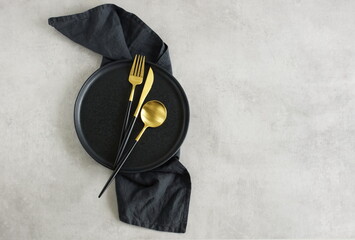 Empty black ceramic plate,linen napkin   and cutlery on gray stone background top view with copy...