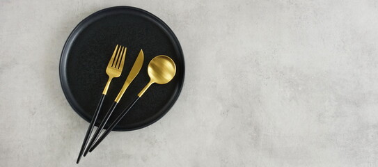 Empty black ceramic plate and cutlery on gray stone background top view with copy space banner ....