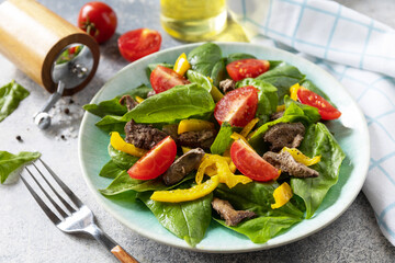 Warm salad of young spinach, chicken liver, tomatoes and grilled peppers with spices and balsamic. Healthy keto diet low carb.