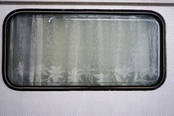Wohnwagenfenster mit wei&szlig;en Gardinen mit Blumenmuster 