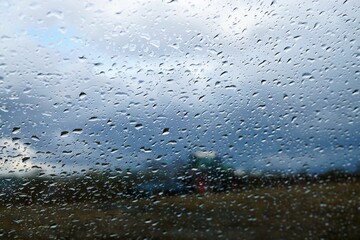 Glasscheibe mit Regentropfenmuster vor Trecker beim Pflügen auf Feld und Himmel bei Regen am Abend...