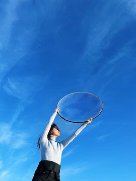 Woman holding a round photographic reflector in her hands against blue sky