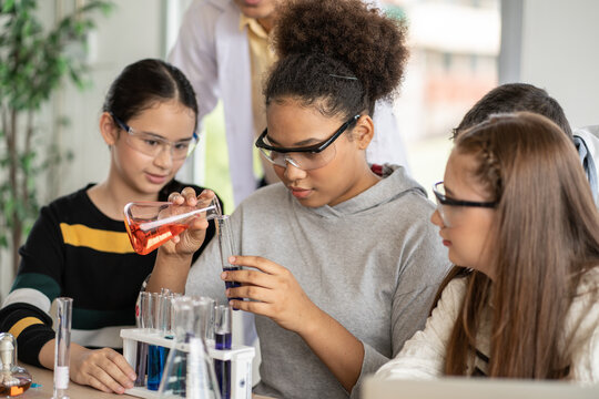 Diversity group of students in protective eyeglasses in science class doing chemical experiment in laboratory. Teacher watching girl mixing chemistry in test tube. learning and education concept