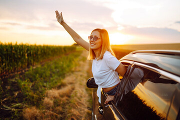 Lifestyle! Happy woman enjoys sunset views from the car window. Young tourist woman rests and leans out of the car window, enjoys the trip. Travel concept, vacation. Towards adventure.