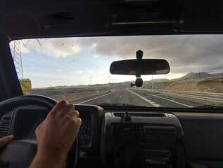 Pov point of view of man hand driving the car in scenic destination long straight roads with mountains around. Concept of transport and drive. People traveling alone. Adventure lifestyle. Vacation