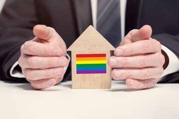 Businessman hand holding wooden Home model with LGBT flag. insurance and property concepts